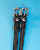 Black leather donkey spur straps with silver buckles on a light blue background