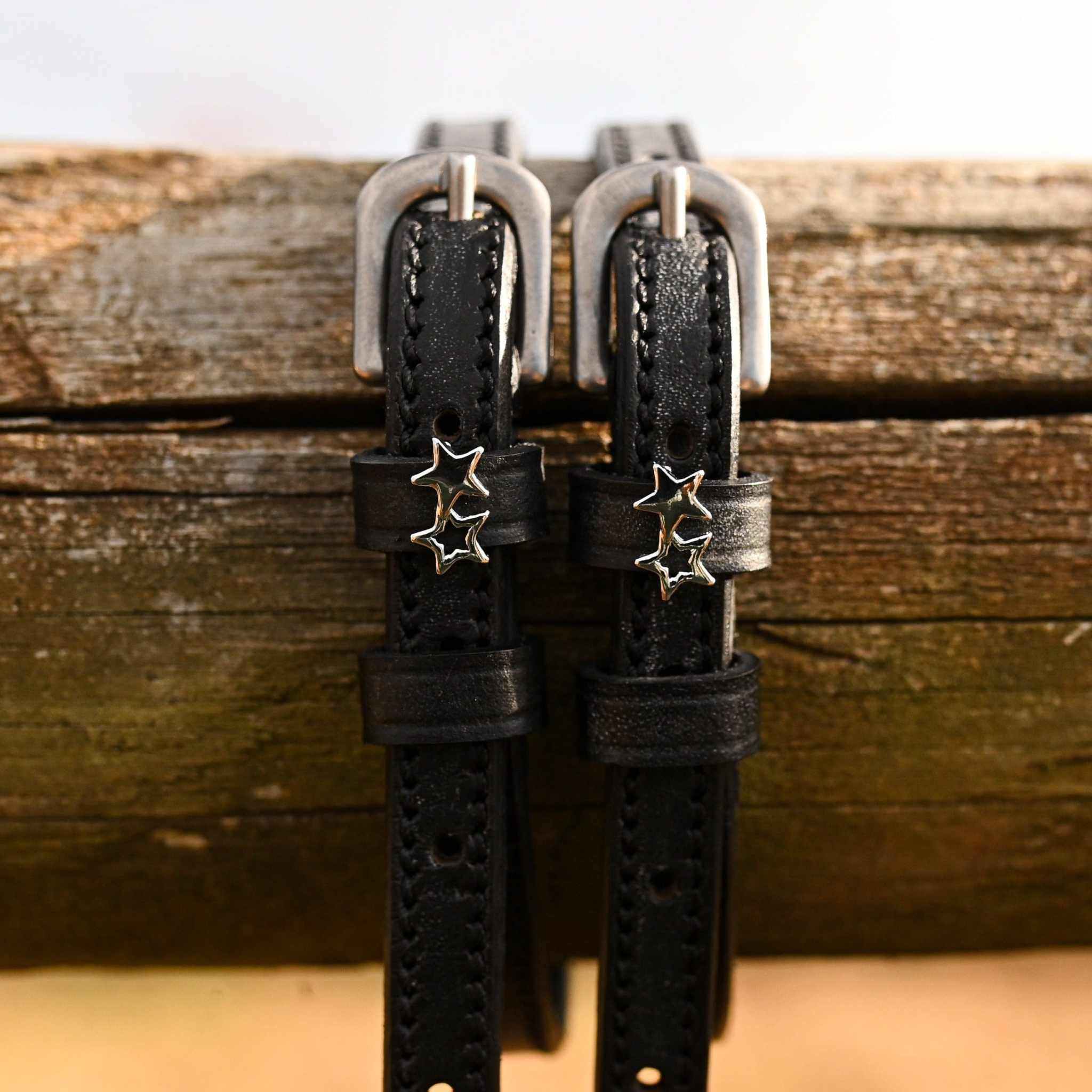 ManeJane double star spur straps hanging over a weathered wooden fence rail