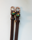 Brown leather dumpster fire spur straps with rose gold buckles on pale blue