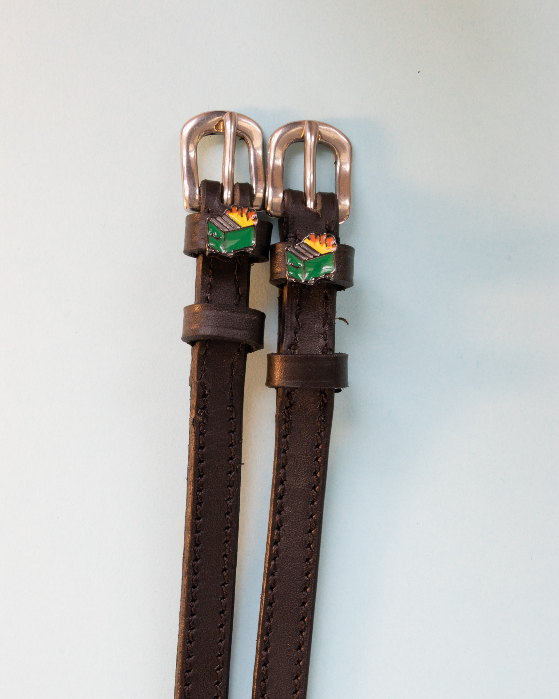 Brown leather dumpster fire spur straps with rose gold buckles on pale blue