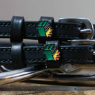 Close-up of green dumpster fire enamel charms on black leather spur strap keepers