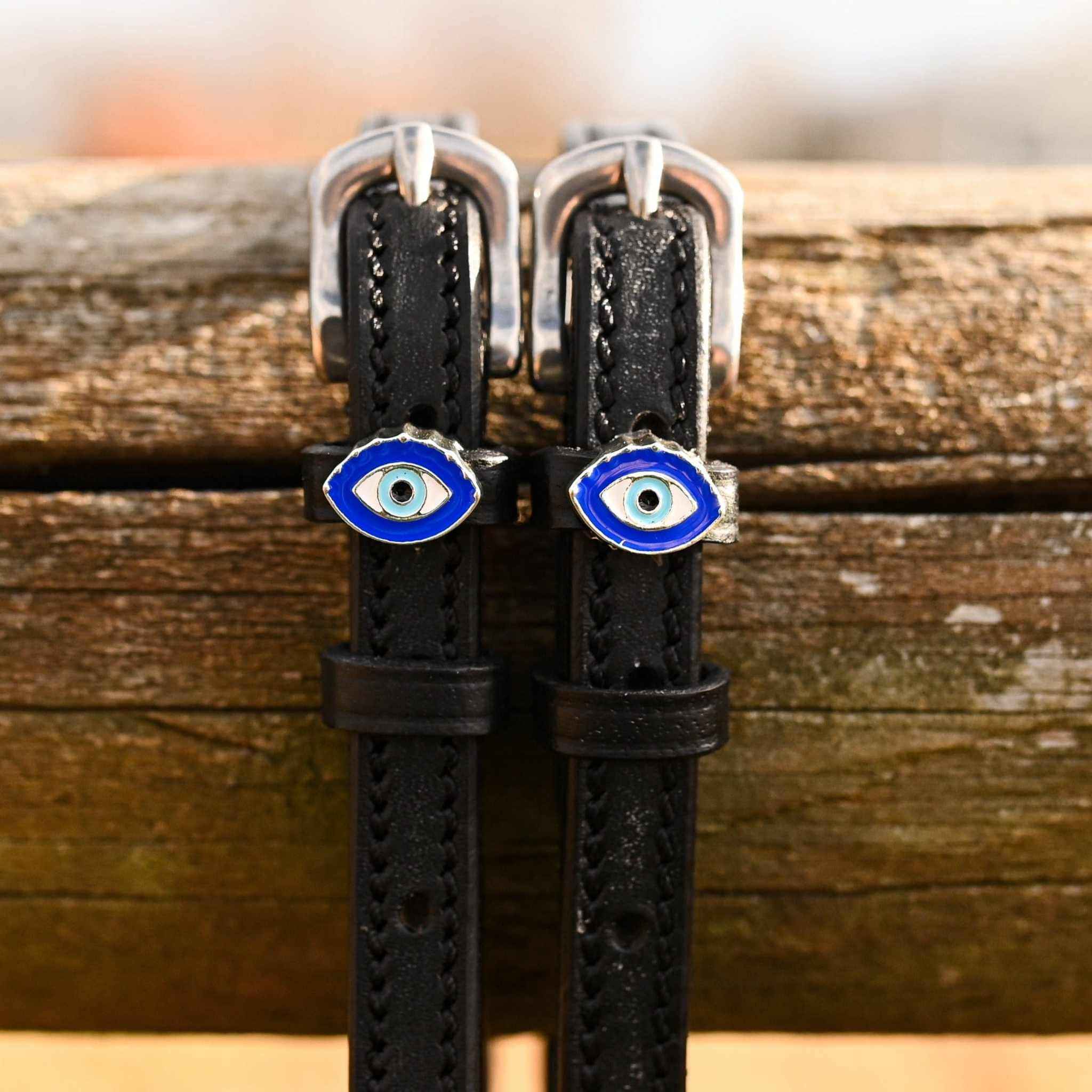 Close-up of blue evil eye charms on black leather spur straps over a wooden rail