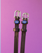 Brown leather ManeJane spur straps with blue evil eye charms on a purple background