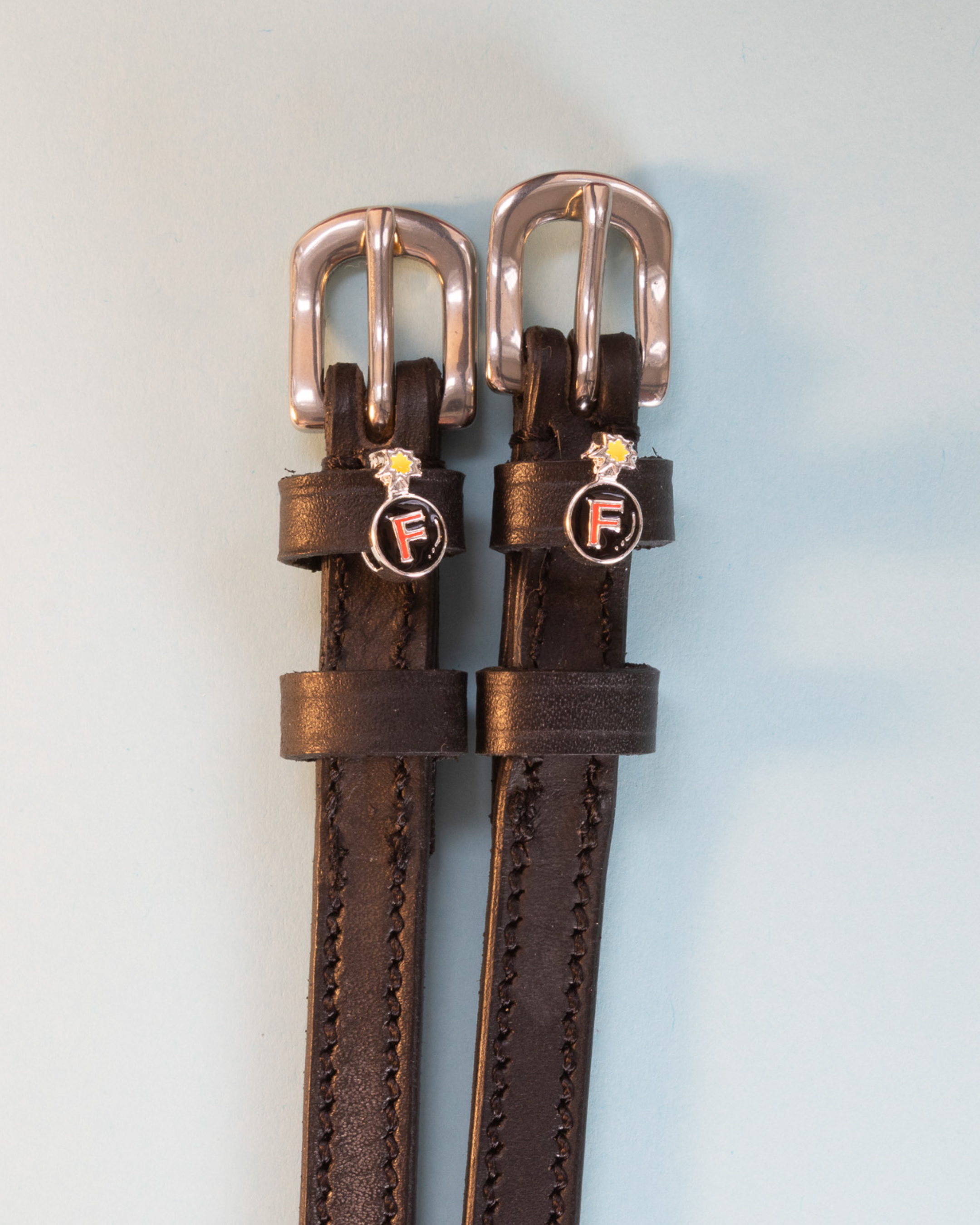 Brown leather F Bomb spur straps with rose gold buckles and bomb charms on pale blue