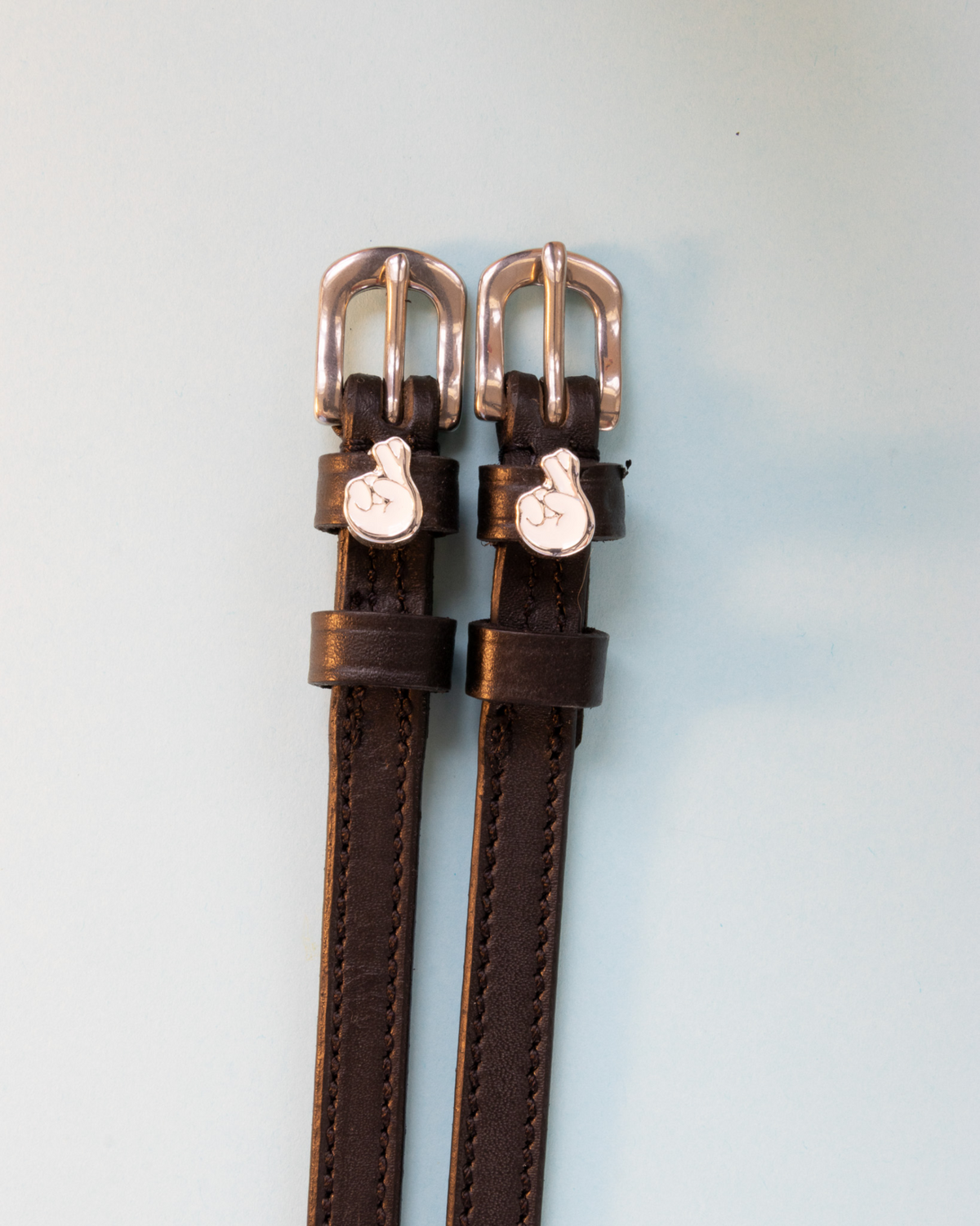 Brown leather ManeJane spur straps with silver buckles and crossed-fingers charms