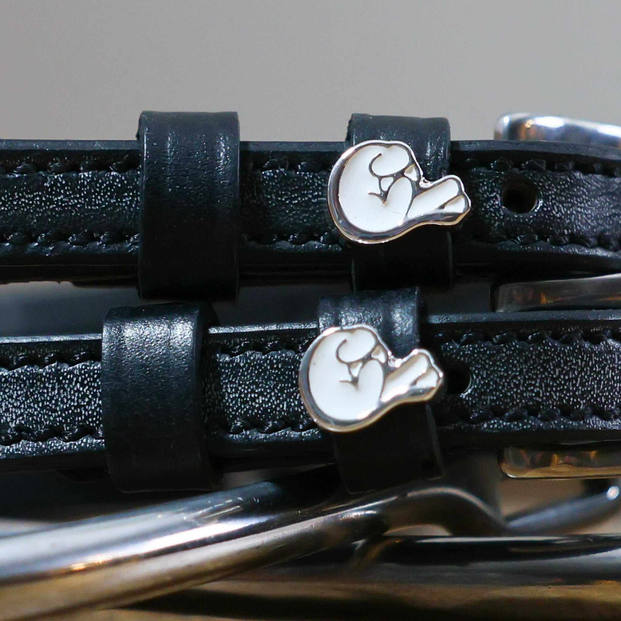 Close-up of white crossed-fingers charms on black leather ManeJane spur strap keepers