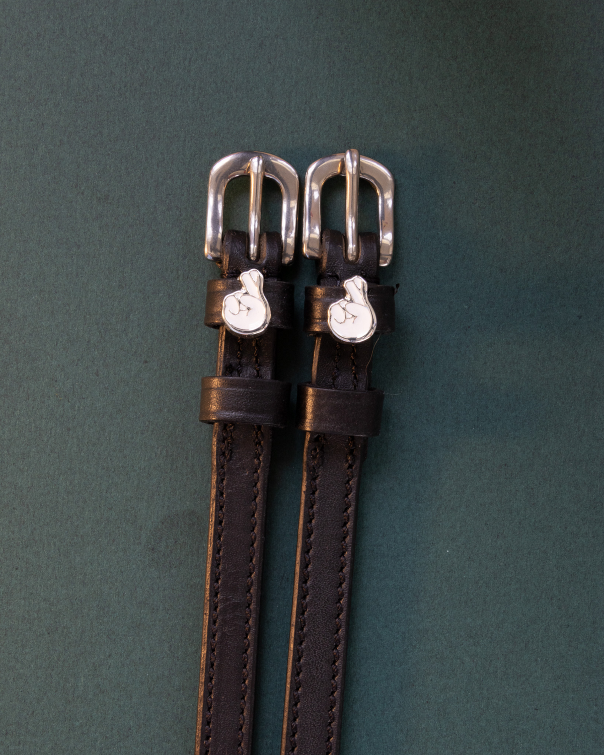Black leather crossed-fingers spur straps laid flat on a dark green background