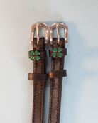 Brown leather ManeJane clover spur straps with rose-gold buckles and green clover charms