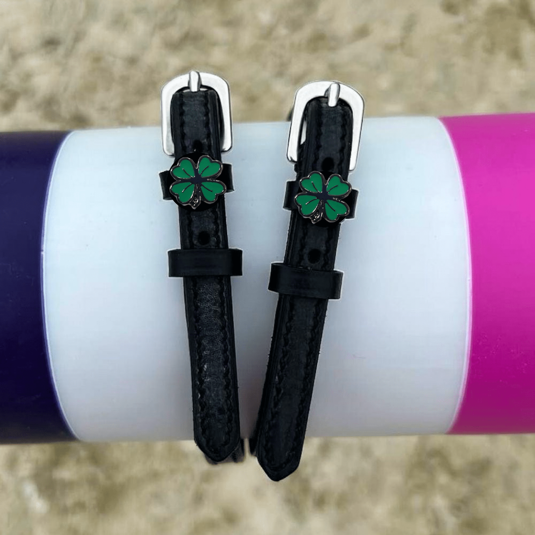 Four leaf clover spur straps draped over a purple and pink jump rail, green clover charms