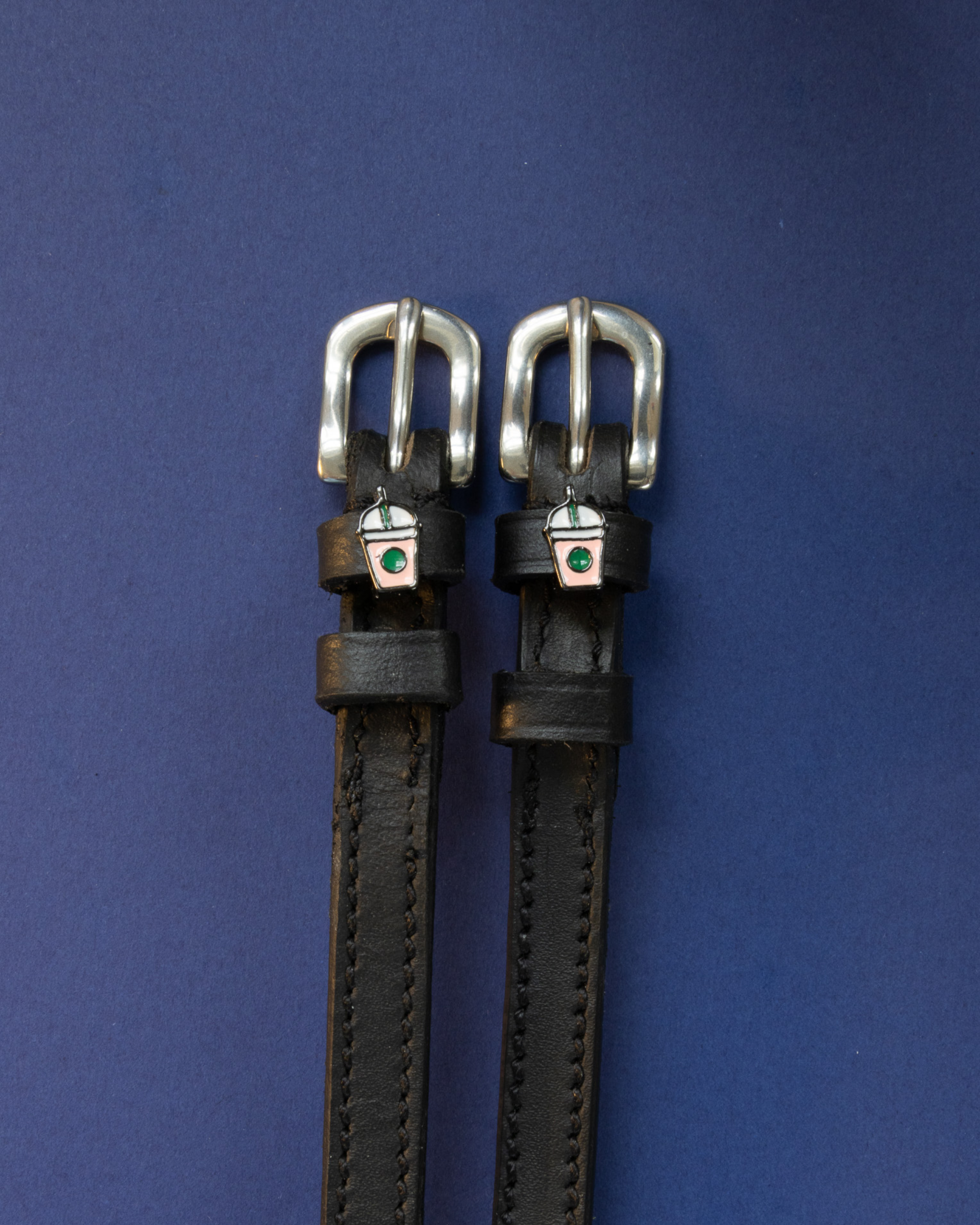Pair of black leather frappe cup spur straps on a navy blue background