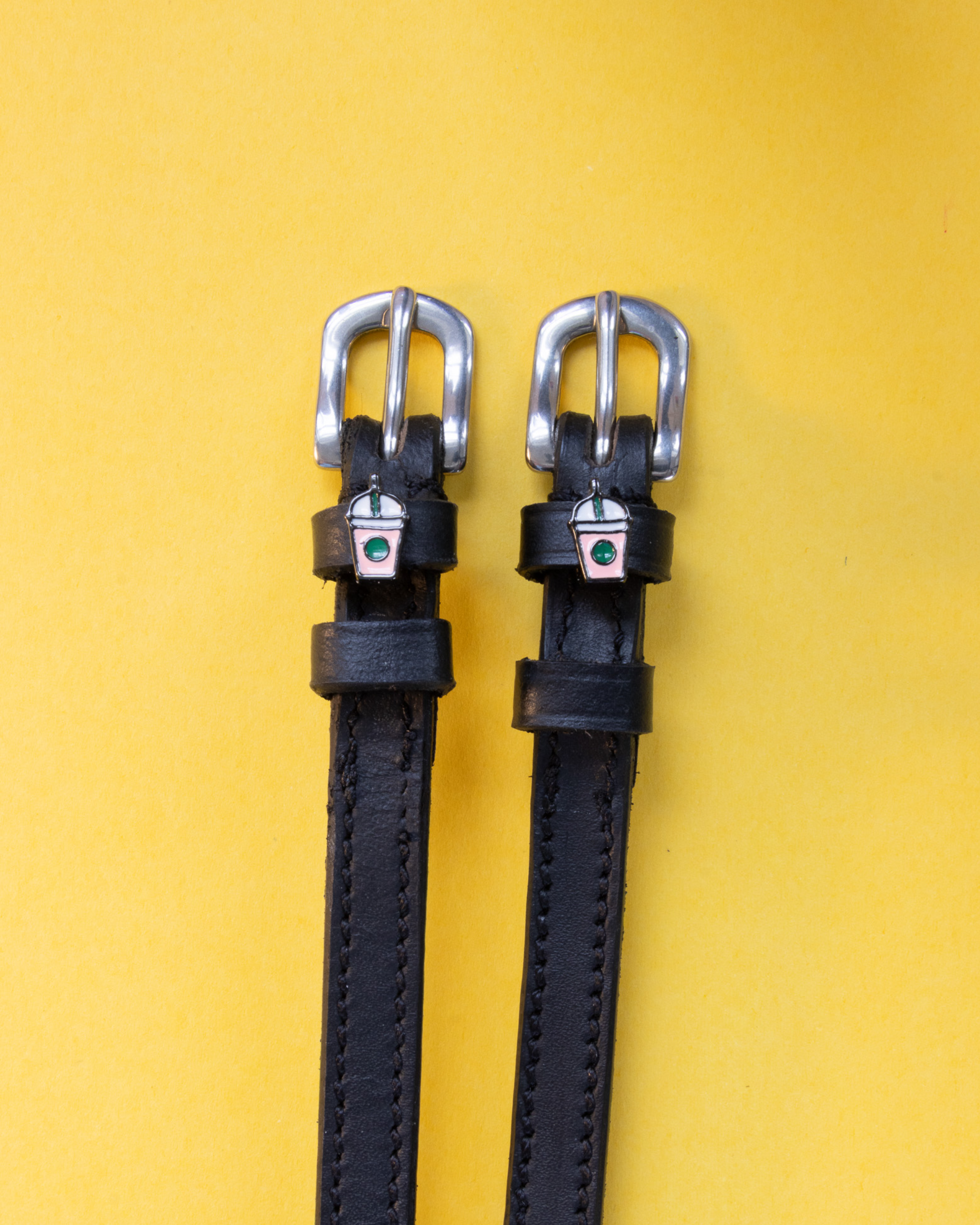 Black leather frappe cup spur straps laid flat on a yellow background
