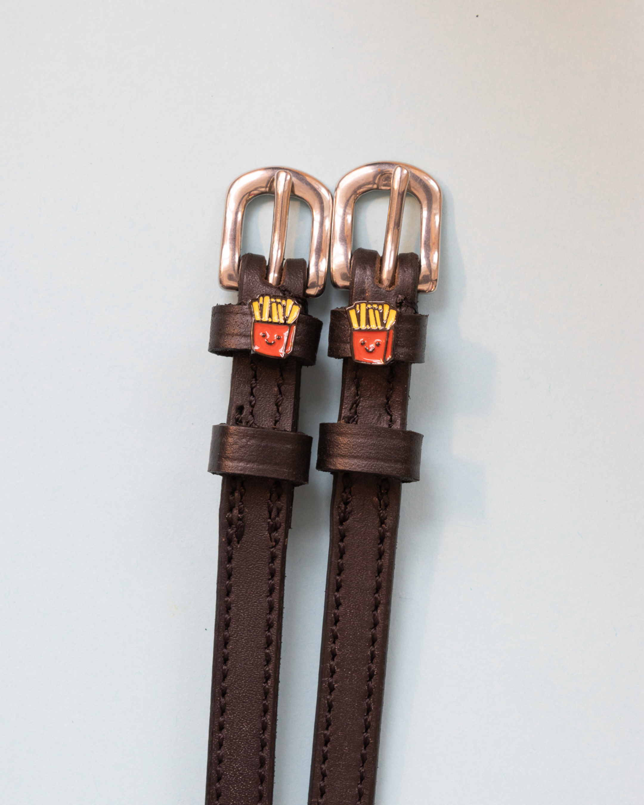 Dark brown French Fries spur straps with rose gold buckles and fry charms on pale grey