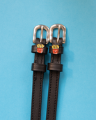Pair of black leather French fry charm spur straps with silver buckles on light blue