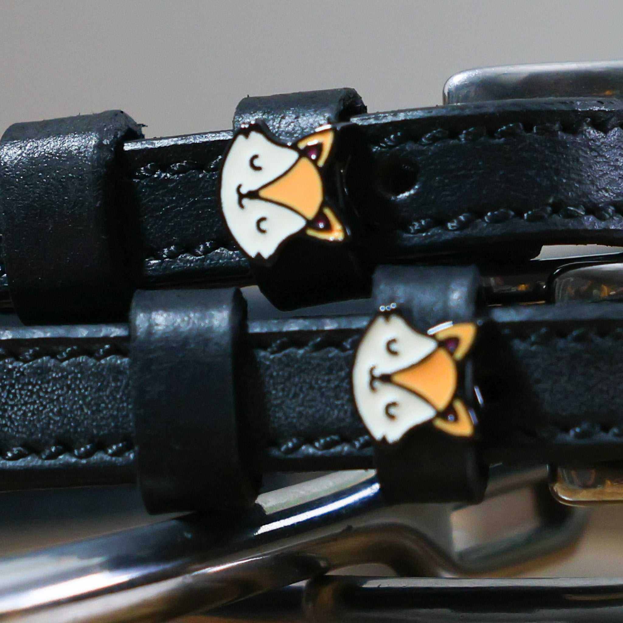 Close-up of orange fox face charms on the keepers of black leather spur straps