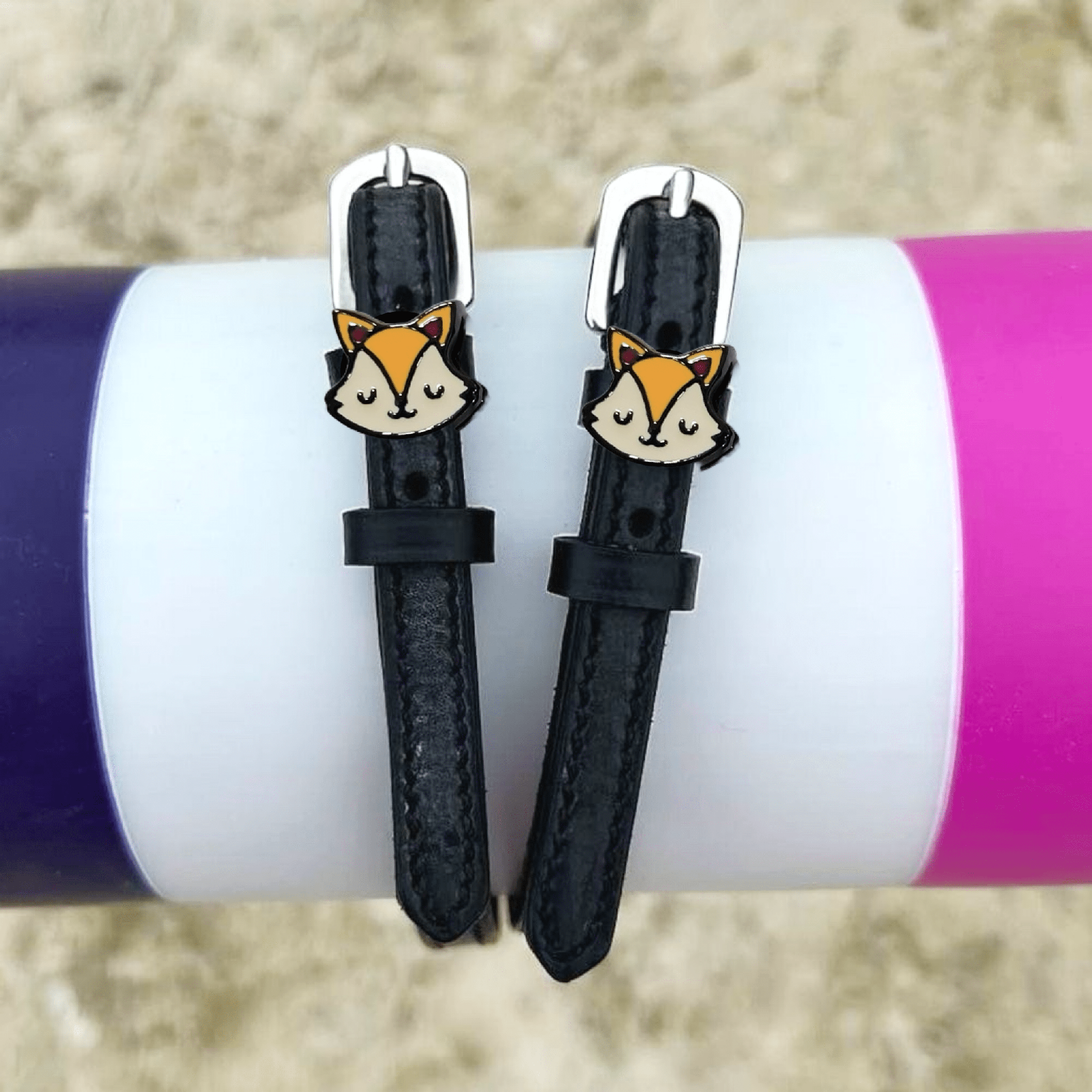 Black leather fox spur straps styled over colorful tumblers on sand by ManeJane