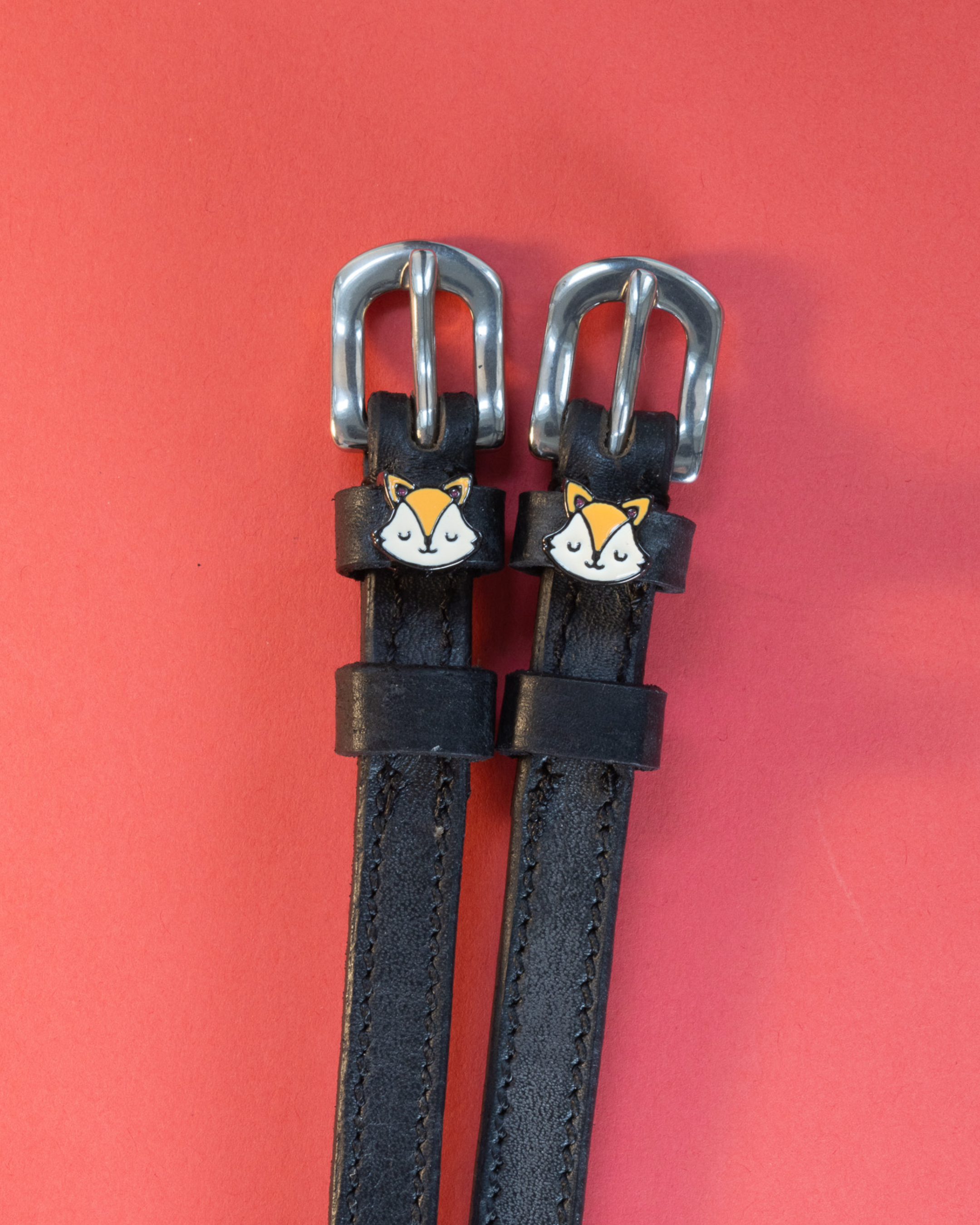 Pair of black leather fox face spur straps with silver buckles on a coral background