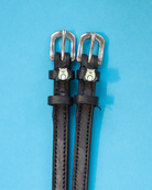 Black leather ManeJane frog spur straps with silver buckles on a light blue background