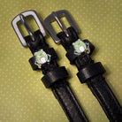 Black leather frog spur straps with silver buckles on a green polka-dot background