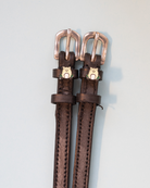 Brown leather ManeJane frog spur straps with rose-gold buckles on a grey background