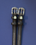 Pair of black leather ManeJane frog spur straps with silver buckles on a deep blue background