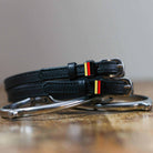 Black leather German flag spur straps coiled beside a silver spur on a wooden surface