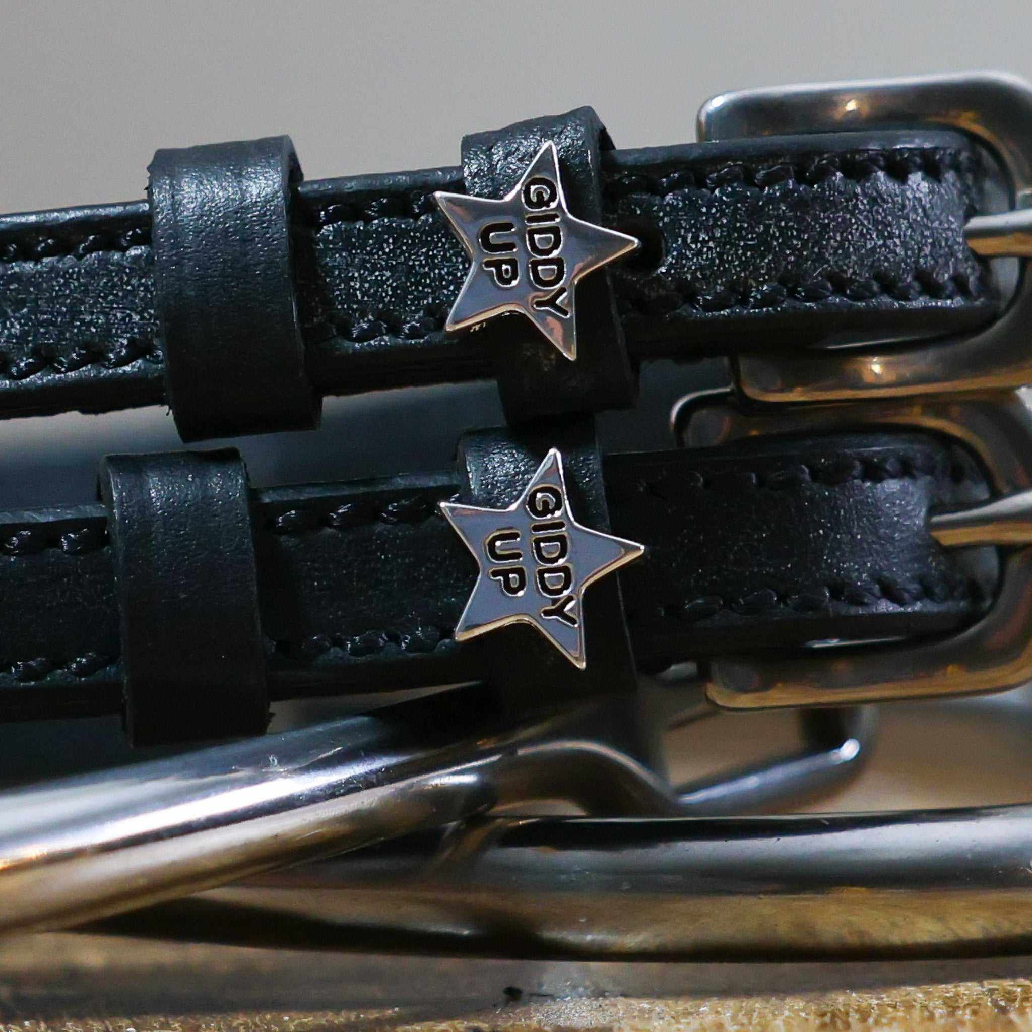 Close-up of silver 'Giddy Up' star charms on black leather spur strap keepers