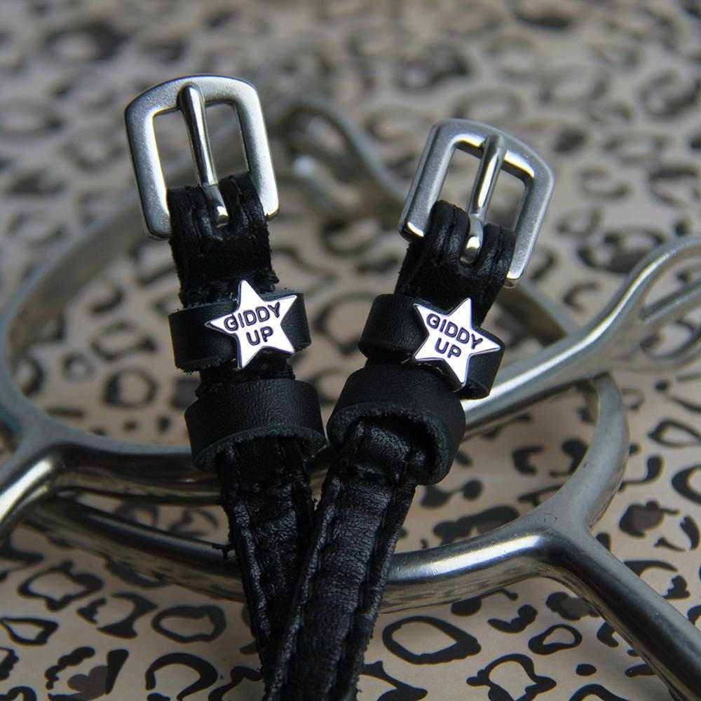 Close-up of black-enamel 'Giddy Up' star charms on spur straps over a leopard print