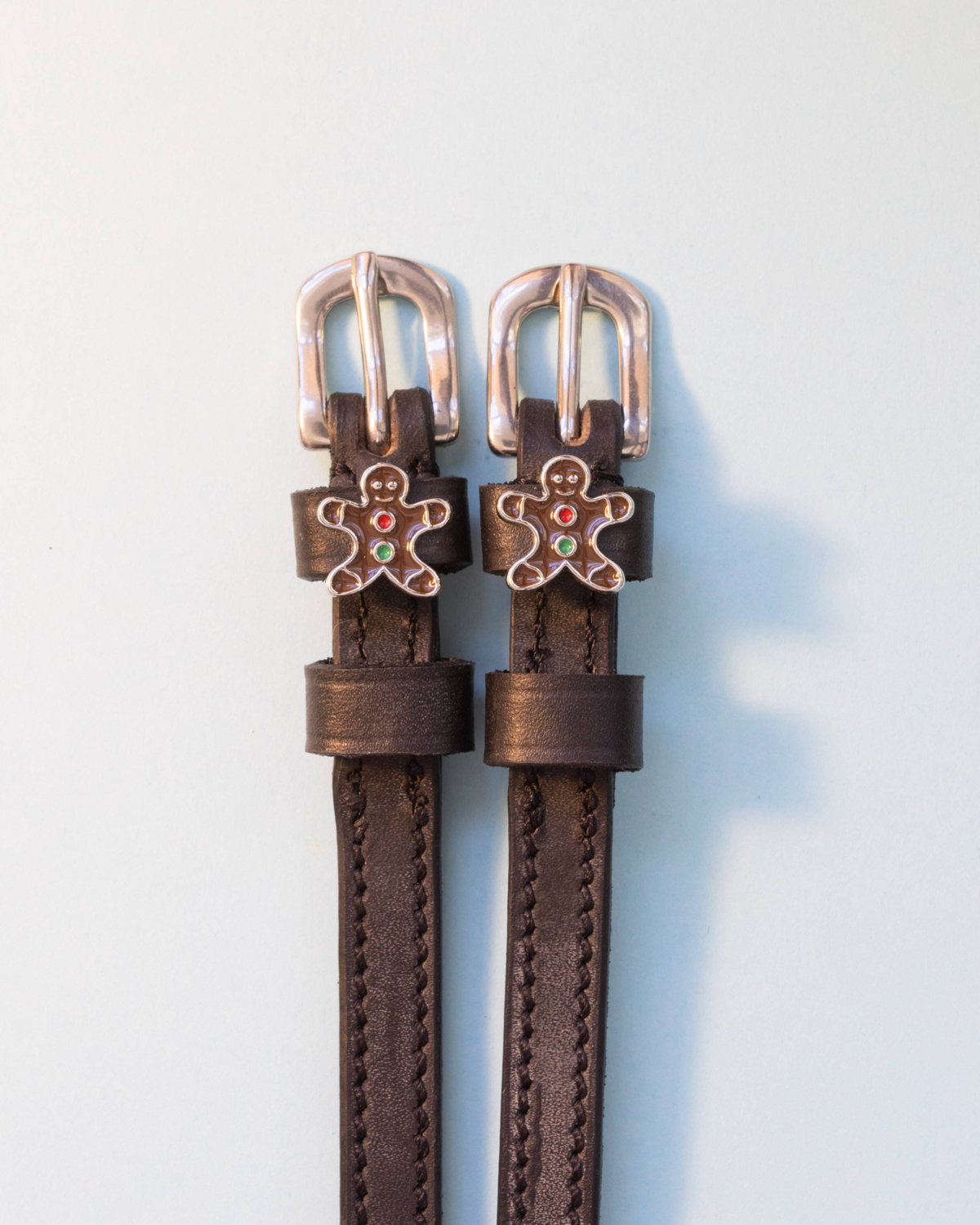 Dark brown leather gingerbread man spur straps with silver buckles on off-white
