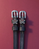 Black leather gingerbread man spur straps flat-laid on a burgundy background