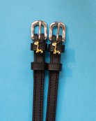 Black leather giraffe charm spur straps with silver buckles on a light blue background