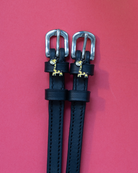Black leather ManeJane Giraffe spur straps with silver buckles on a red background