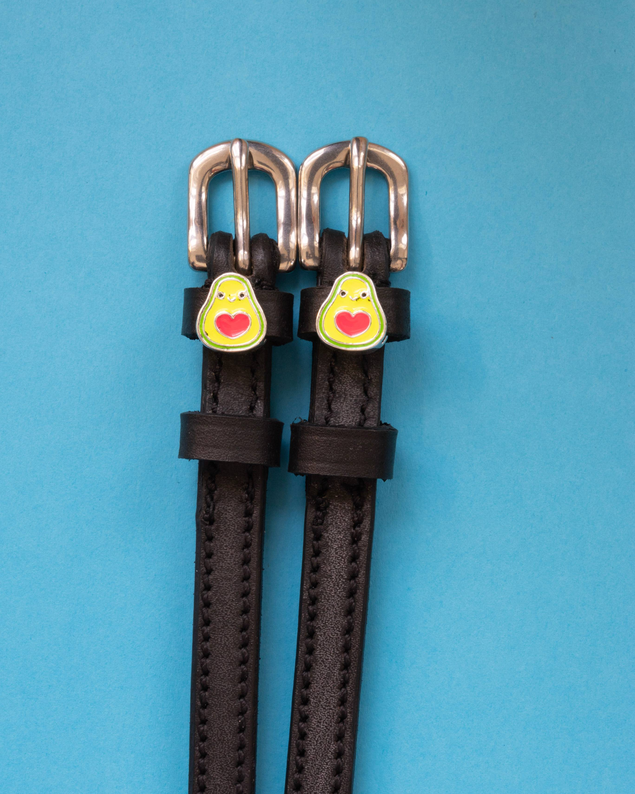 Happy avocado spur straps in black leather laid flat on a blue background