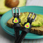 Avocado-charm ManeJane spur straps resting on avocado toast on a teal plate