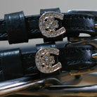Close-up of rhinestone horseshoe-and-clover charms on black leather spur strap keepers
