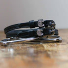 Coiled black leather spur straps with sparkling horseshoe-clover charms stacked on a spur