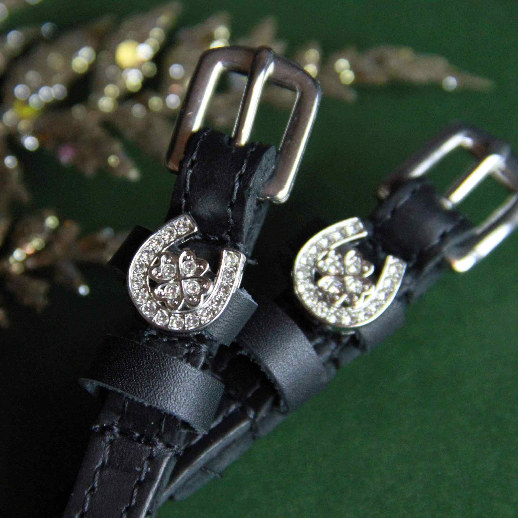 Close-up of crystal horseshoe-clover spur strap charms with dark buckles on green