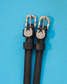 Pair of black leather horseshoe clover spur straps with crystal charms on light blue