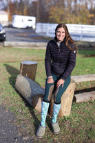 Woman sitting on log wearing Limited Edition Pony Island Pony Transport Socks with pony design in outdoor setting