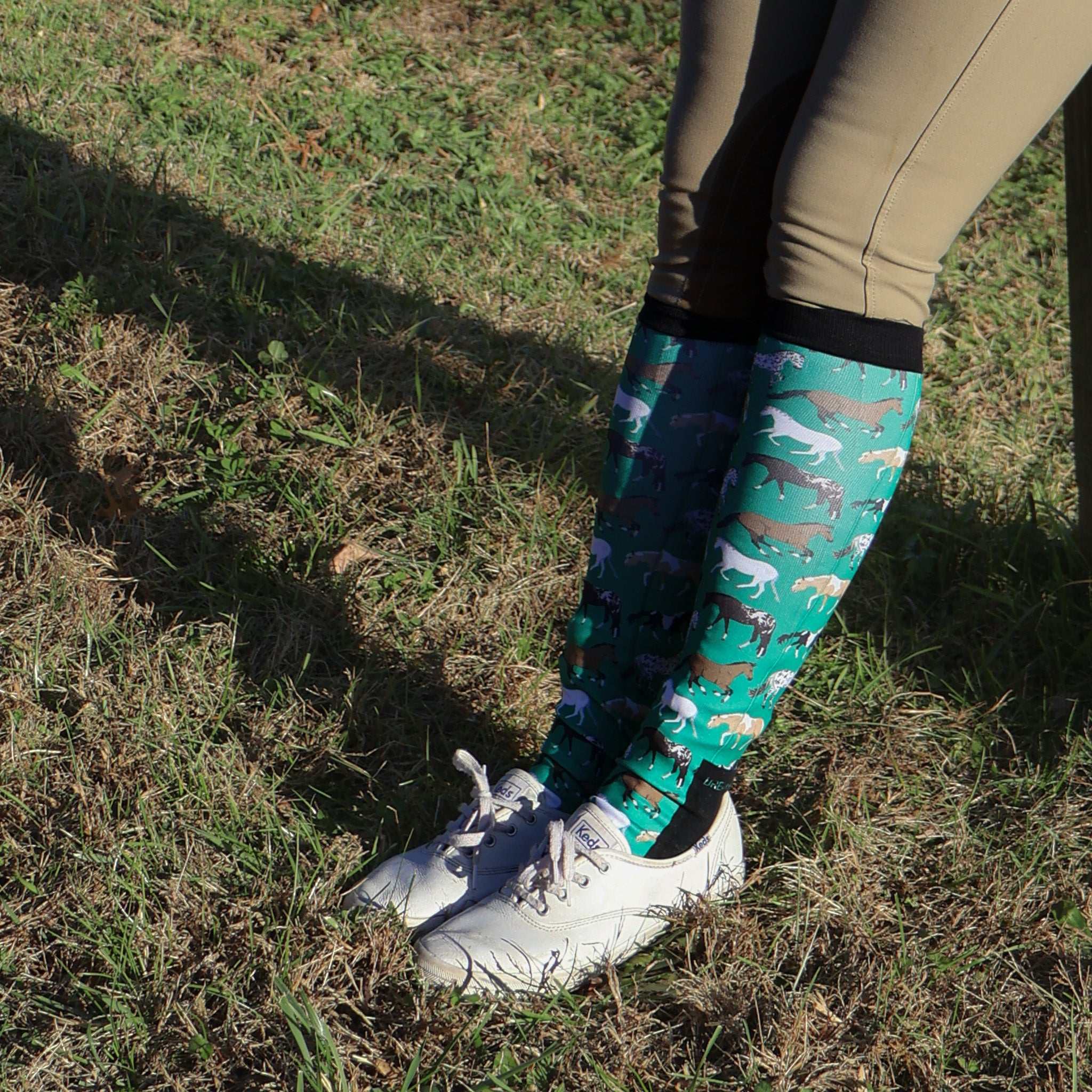 Limited Edition Pony Island green boot socks with horse pattern worn with riding pants and white sneakers outdoors