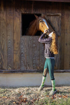 Young rider wearing Limited Edition Pony Island Neon Ponies Socks petting a horse at a stable