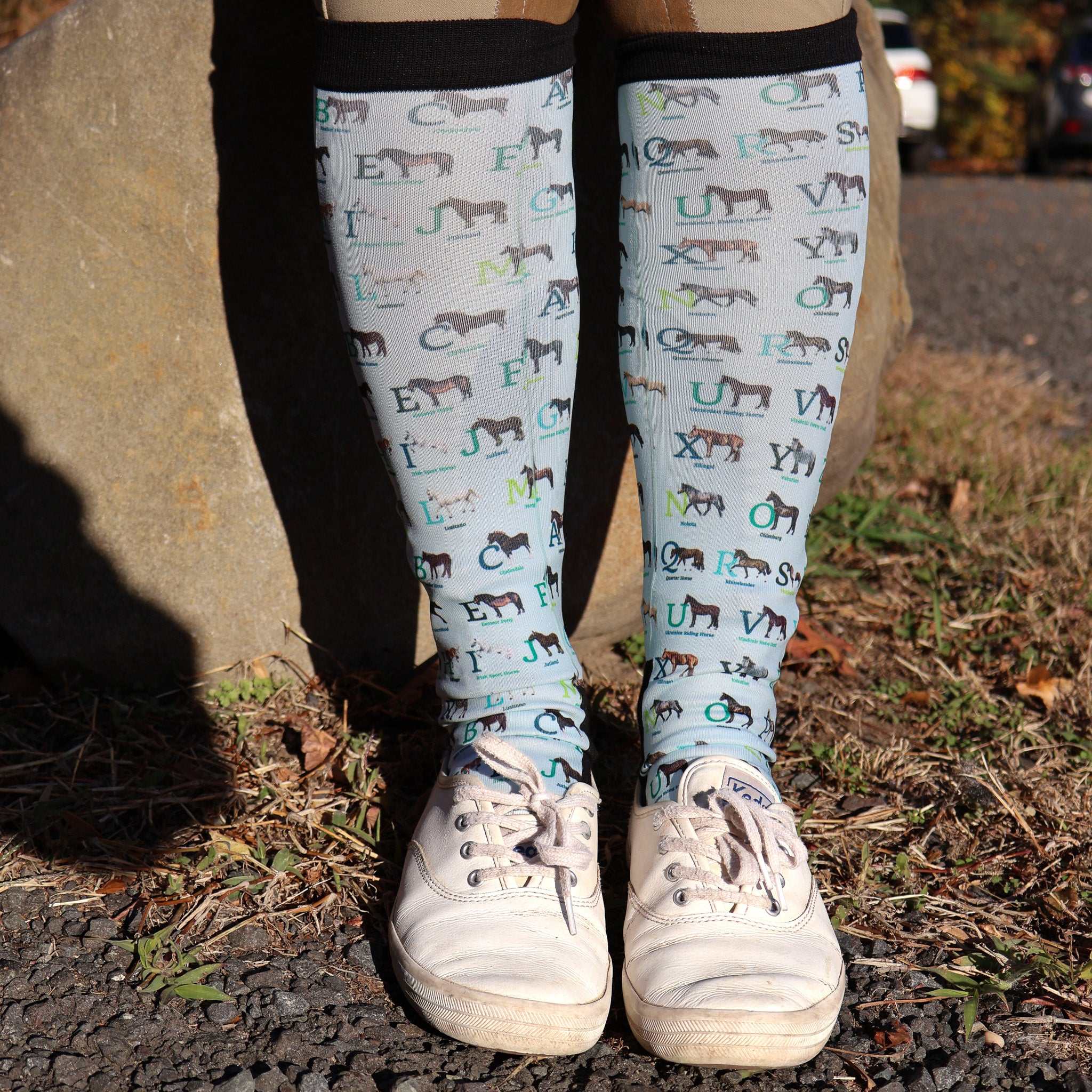 Limited Edition Pony Island Alphabet Horses socks featuring colorful horse-themed ABC design on knee-high socks worn with white sneakers outdoors