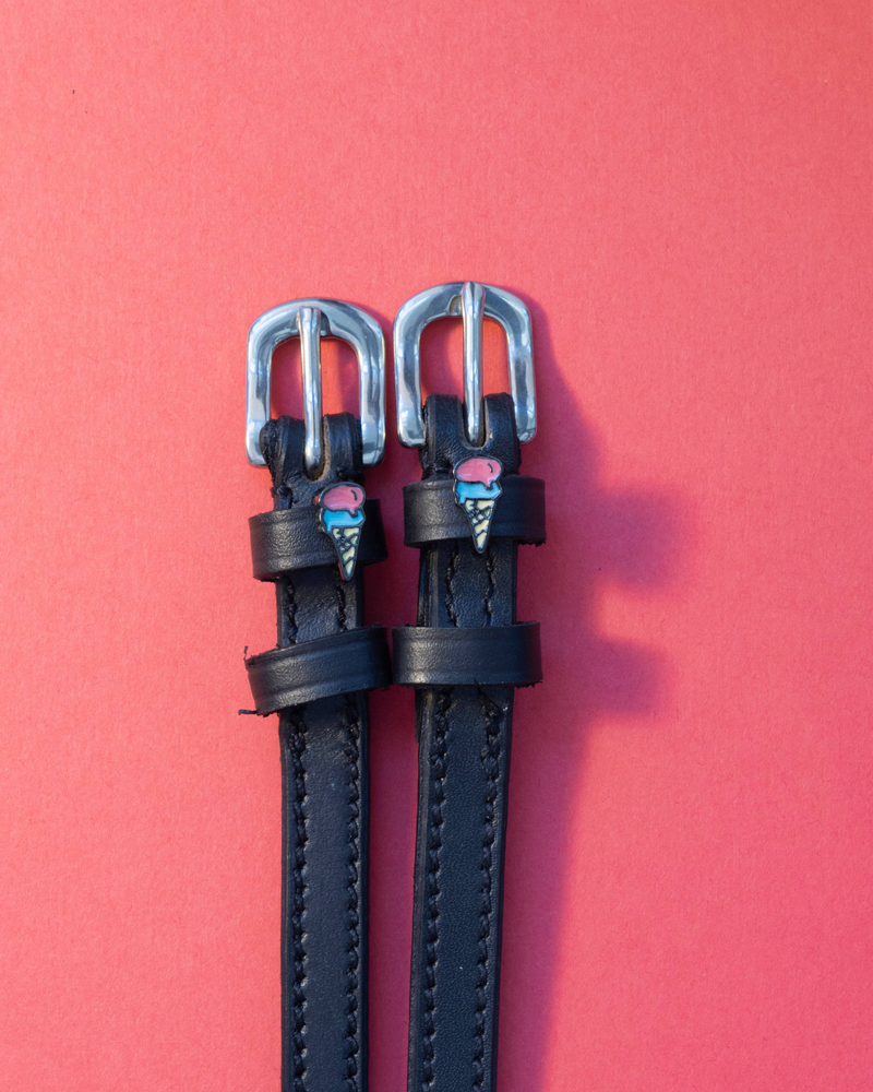 Black leather ManeJane spur straps with ice cream cone charms on a coral background