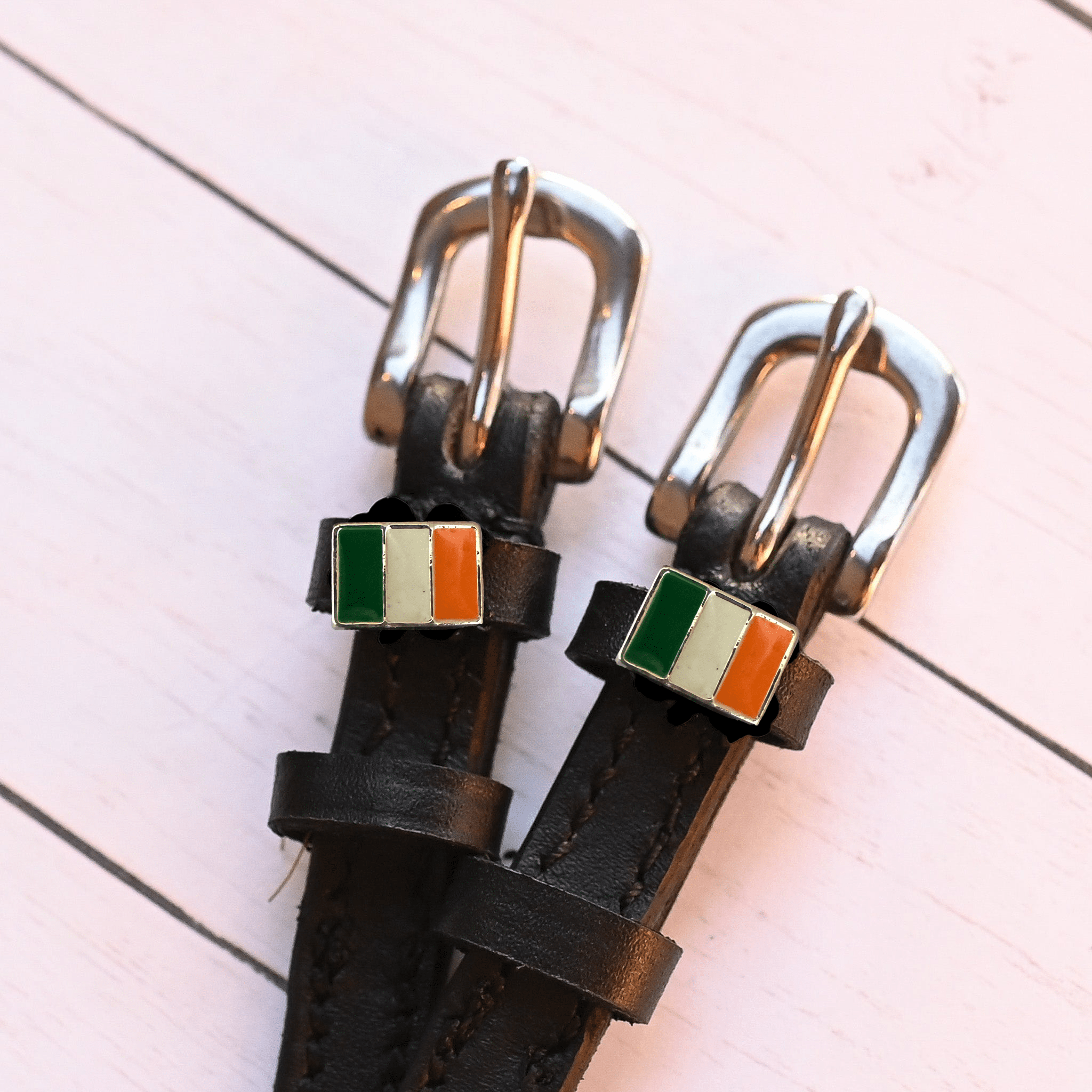 Angled close-up of Irish flag charms on ManeJane spur straps over pink planks