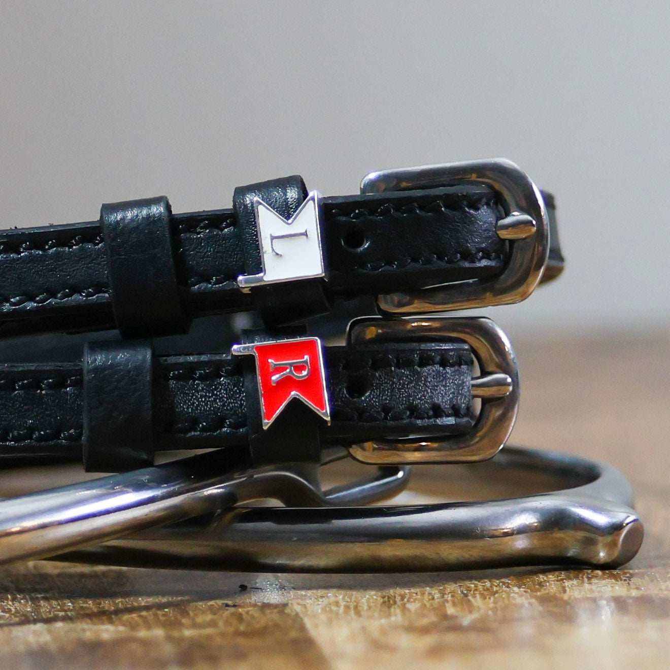 Close-up of white L and red R jump-flag charms on black leather ManeJane spur straps