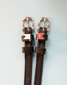 Brown leather ManeJane jump-flag spur straps with rose-gold buckles on pale blue