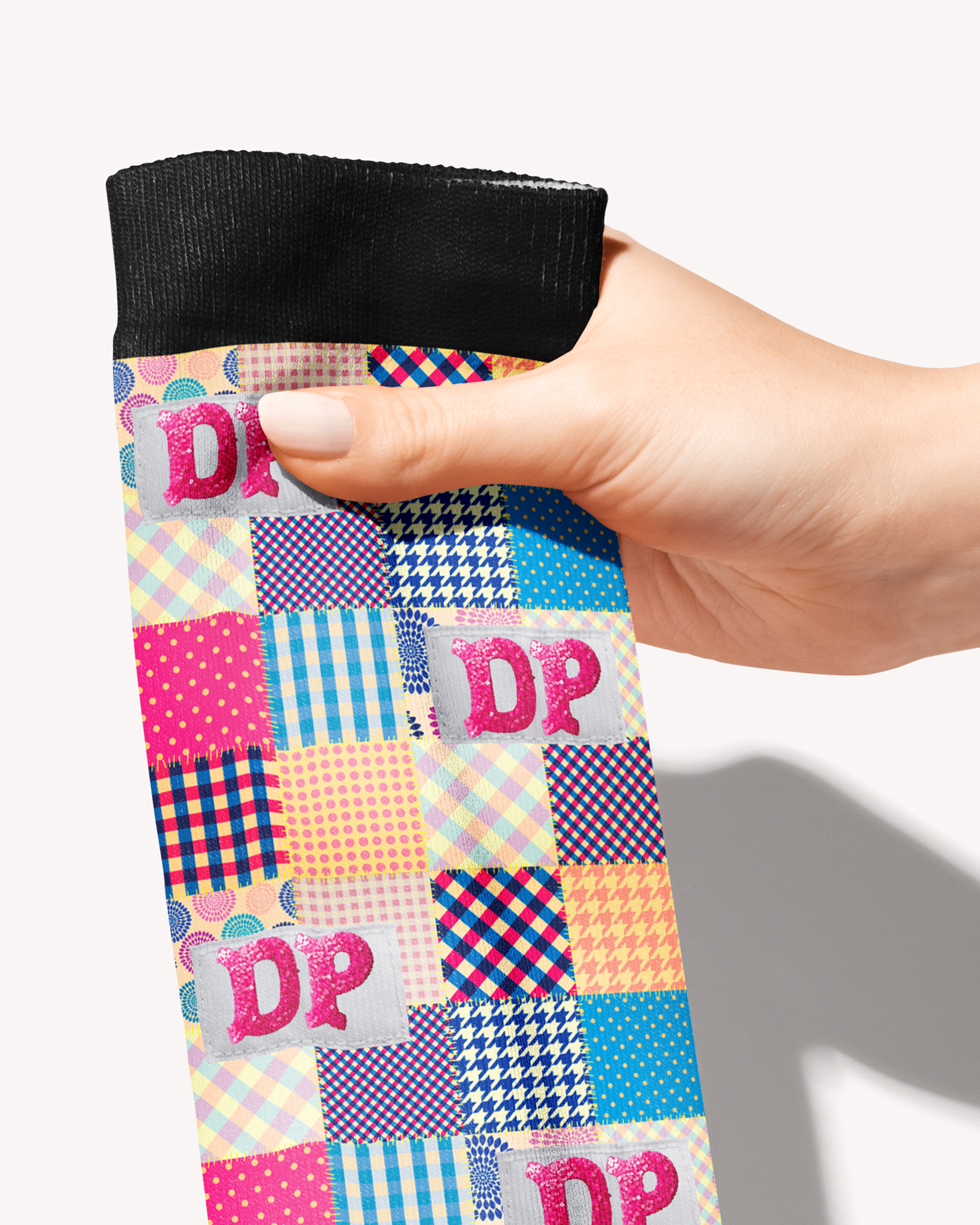 Close-up of the Socks of Many Colors patchwork print, gingham and dot squares with a pink DP monogram