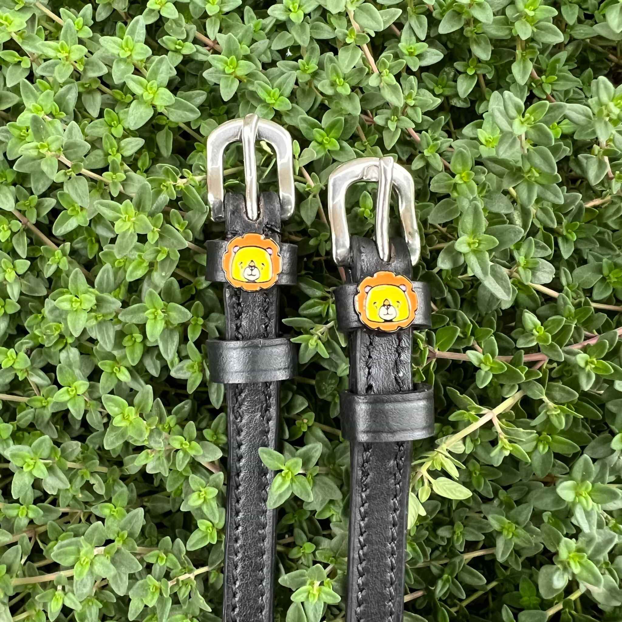 Black leather ManeJane lion spur straps set against green garden foliage