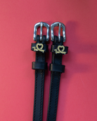Black leather Long Dogs spur straps with gold dachshund charms on a coral background