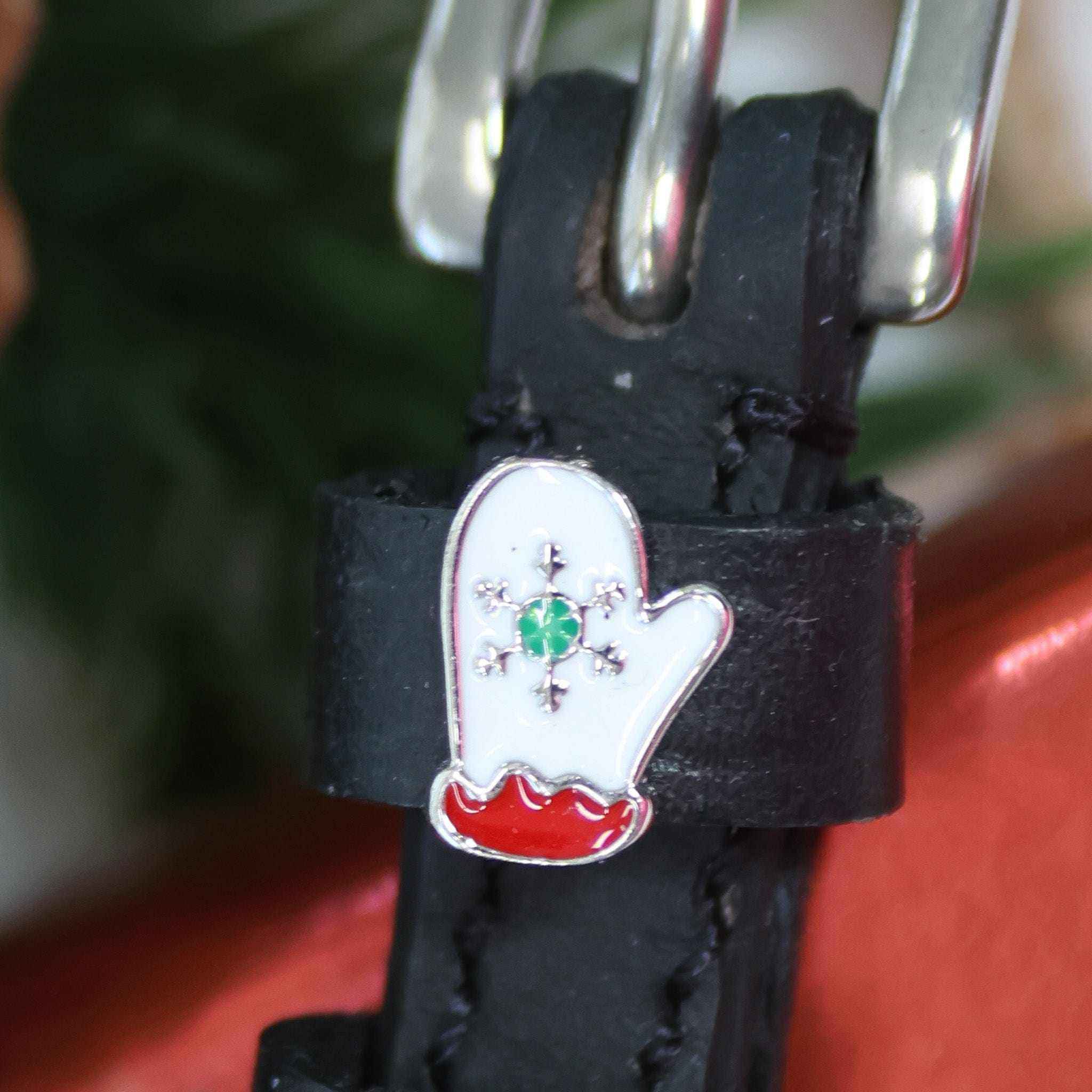 Extreme close-up of a white mitten charm with green snowflake on a black leather spur strap