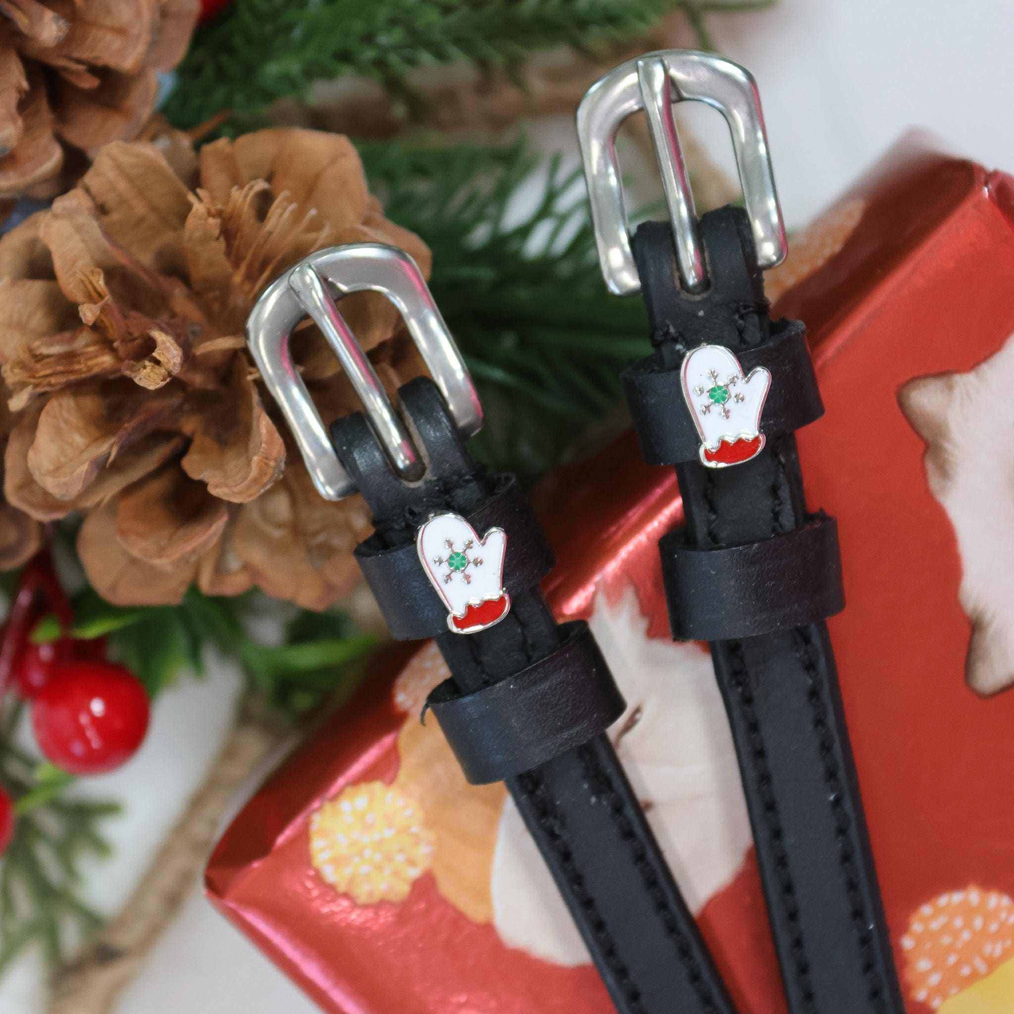 Black leather ManeJane mitten spur straps with silver buckles beside a red holiday gift